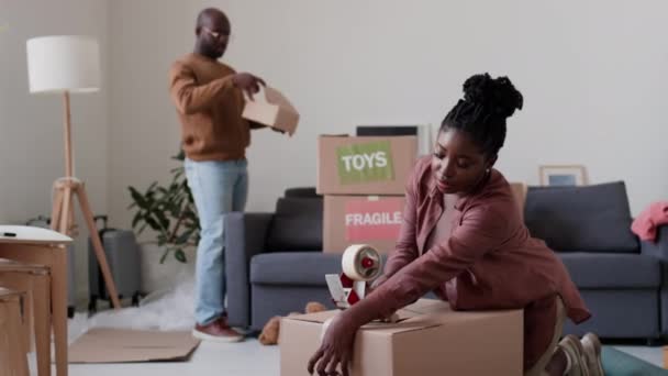 Afroamerykanka Uszczelnianie Kartonowe Pudełko Salonie Podczas Pakowania Rzeczy Rodziną Przeprowadzki — Wideo stockowe