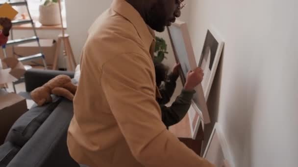 Padre Afroamericano Sosteniendo Niño Colgando Cuadro Enmarcado Pared Sala Estar — Vídeo de stock