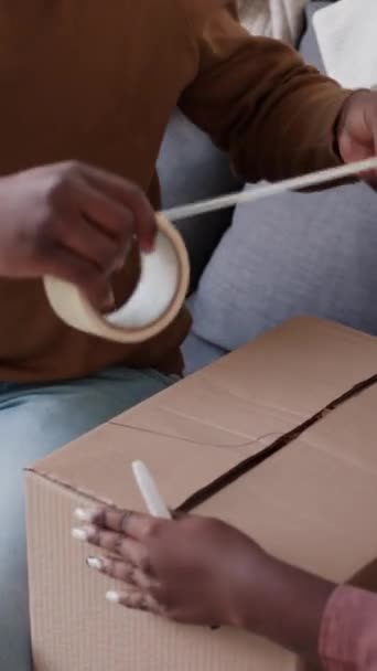 移動のための荷物を詰めている間接着テープが付いているアフリカ系アメリカ人の家族のシーリング ボール紙箱の縦の閉鎖のショット — ストック動画