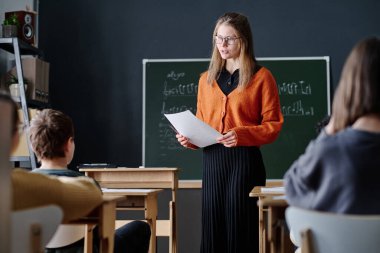 Orta boy beyaz kadın öğretmen ders sırasında çocuklara müzik teorisini açıklarken.