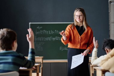 Seçici odak noktası, genç beyaz bir kadının okulda çocuklarla çalışırken müzik öğretmesi.