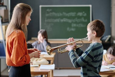 Genç müzik öğretmeninin önünde duran öğrenci okulda trompet çalışıyor, seçici odak atışı.