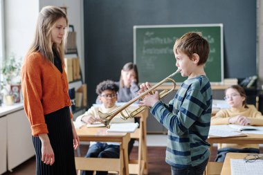 Genç bayan müzik öğretmeni ve çocukların sınıfta trompet çalan çocuğu dinlerken seçmeli odak noktası.