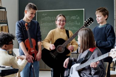 Bir grup neşeli genç kız ve erkek müzik aletleri ile sınıfta prova yaparken mola veriyorlar.