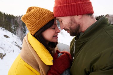 Birbirine aşık erkek ve kadının, kış günü gözleri kapalı ve el ele tutuşmuş bir fotoğrafı.