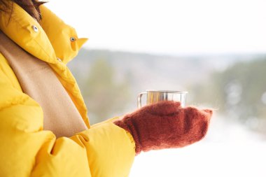 Soğuk bir kış günü elinde bir fincan sıcak çayla dışarıda duran tanınmayan bir kadın.