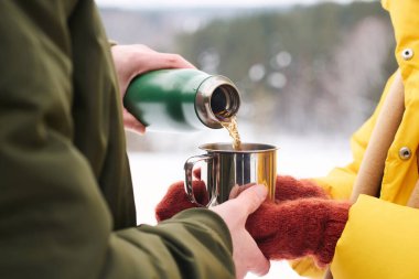 Tanımlanamayan erkek turist, soğuk kış gününde karısı için sıcak çayı bardağa dolduruyor.