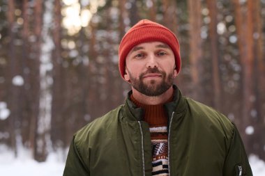 Kışın ormanda duran, kalın kıyafetler giyen beyaz bir adamın portresi.