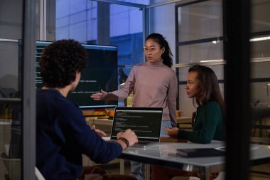 Etnik çeşitlilikte programcılar akşam geç saatlerde bilişim şirketinin ofisindeki iş yerinde kod üzerinde birlikte çalışıyorlar.