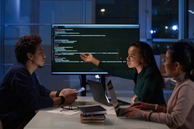 Üç genç etnik çeşitlilikte programcıdan oluşan bir grup geceleri ofiste kod üzerinde birlikte çalışıyorlar.