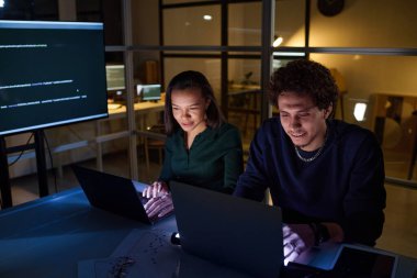 Gece geç saatlerde iş yerindeki bilgisayarlarda kodlama yapan etnik çeşitlilikteki genç programcıların yüksek açılı görüntüsü