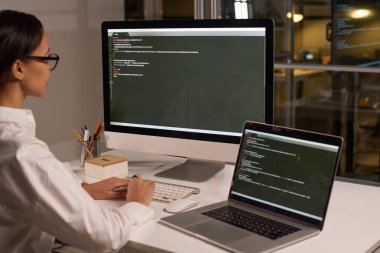 Modern genç bayan programcı akşam geç saatlerde modern ofiste bilgisayar üzerinde kod yazma geliştiriyor.