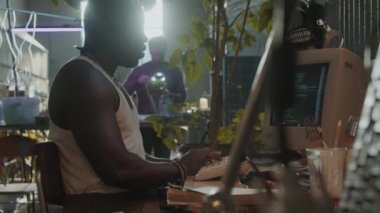 Siyahi adam, kıyamet sonrası sığınakta hayatta kalanlarla yaşarken masada oturup bilgisayarında program kodları yazıyor.