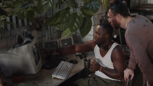 年轻的黑人男性幸存者手持钢制杯子 与朋友讨论后启示录地堡中的旧电脑代码 — 图库视频影像