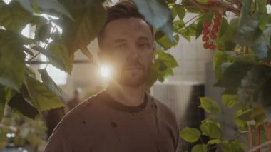 Yeşil bitkilerin arasında dikilen ve kıyamet sonrası sığınakta hayatta kalırken kameraya bakan giysili bir adamın portresi