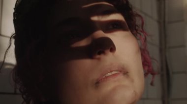 Yüzü kirlenmiş genç pembe saçlı kızın kıyamet sonrası sığınakta beklerken parmaklarının arasından ışığa bakarken yakın plan fotoğrafı.