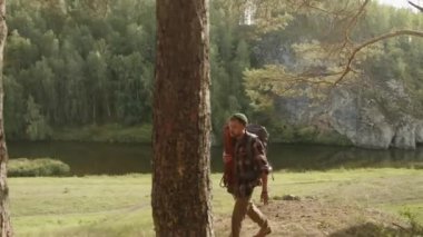 Sırt çantalı ve dağ ekipmanlı genç adam ve kadın yaz yürüyüşü sırasında çam ormanlarında yürüyorlar.