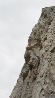 Yazın dağcılık yaparken kayalık kayalıklara tırmanan koruyucu kasklı erkek dağcının dik açılı görüntüsü.