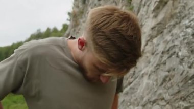 Genç sakallı adamı yukarı kaldır tırmanma takımlarını kontrol et, yukarı bak ve kayaya doğru git.