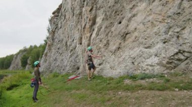 Zoom 'da bir adam kayaya tırmanıyor, sürgüyü kayaya sokuyor ve kız arkadaşı yerde dururken ipi hızlı çekime bağlıyor.