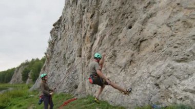 Koruyucu miğferli ve koşumlu bir adam dik kayayı indiriyor ve kız arkadaşına beşlik çakarken doğada dağ tırmanışının keyfini çıkarıyor.