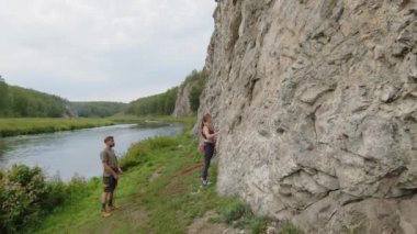 Genç sporcu kadın kayaya tırmanırken erkek arkadaşı yerde duruyor ve ipini tutuyor.
