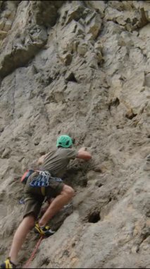 Korumalı miğferli bir adamın kaya yüzeyine tırmanırken, kadın partnerin yerde ip tutarken geniş açılı görüntüsü.