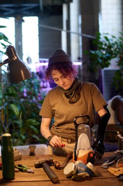 Masa lambasının önünde protez kollu genç beyaz bir kadının dikey orta pozu. Kıyamet sonrası yaşam tarzı kavramı.