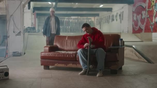Junger Mann Sitzt Auf Couch Indoor Skatepark Und Fixiert Bolzen — Stockvideo