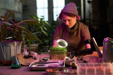 Kıyamet sonrası laboratuarında protez kollu genç bir kadının bitkileri büyütürken orta boy fotoğrafı.