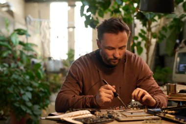 Kafkasyalı teknisyen sıkıntılı bir kazak giyiyor eski bilgisayarı lehimleme demiriyle onarıyor