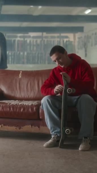 Verticaal Schot Van Jonge Skateboarder Zittend Oude Bank Bij Indoor — Stockvideo