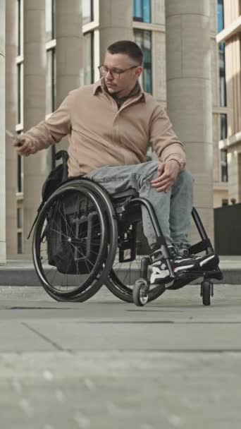 坐在轮椅上的男子从背包里拿起手机接市中心街上电话的垂直镜头 — 图库视频影像