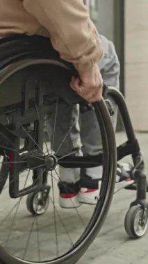 Kentsel cadde boyunca tekerlekli sandalyede oturan adamın dikey yakın çekimi.