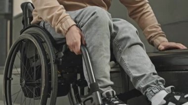 Engelli bir adamın tekerlekli sandalyeden kalkıp şehir caddesinde yedek kulübesine geçişini yakından çek.