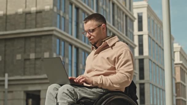 Tekerlekli Sandalyede Dizüstü Bilgisayarda Yazan Genç Bir Adam Şehirdeki Sokakta — Stok video