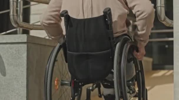 市内の昼間のオフィスビルの前にランプで車椅子に乗る男 — ストック動画