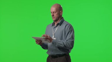 Dijital tablet kullanan orta yaşlı veri merkezi çalışanının portresi ve stüdyodaki yeşil krom anahtar duvara karşı kamera önünde poz vermek