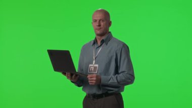 Veri merkezi mühendisinin elinde dizüstü bilgisayar olan portresi ve stüdyoda yeşil krom anahtar arka planda kamera önünde poz veriyor.