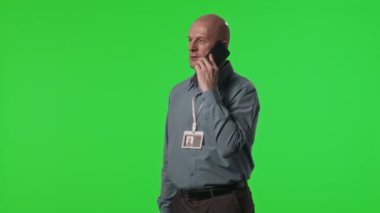 Veri merkezi mühendisinin krom anahtar yeşil duvara karşı duran ve cep telefonuyla konuşan stüdyo görüntüsü.