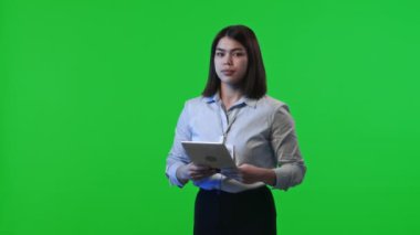 Dijital tablet tutan kadın veri merkezinin portresi, kameraya dönüyor ve stüdyoda krom anahtar yeşil arka planda poz veriyor.
