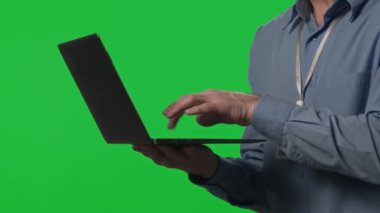 Erkek veri merkezi teknisyeninin elinde dizüstü bilgisayar tutarken ve stüdyoda yeşil renkli ekranda yazarken görüntüsünü kapat.