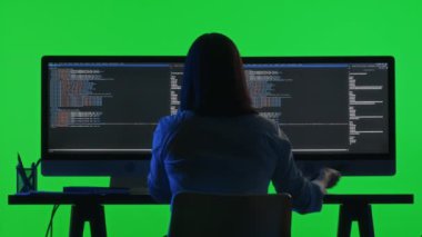 Kahve içen ve telefonuna cevap veren kadın programcının arka planı. Stüdyodaki yeşil renkli anahtar arka planına sahip çift monitörlü bilgisayarda kodlama yaparken.