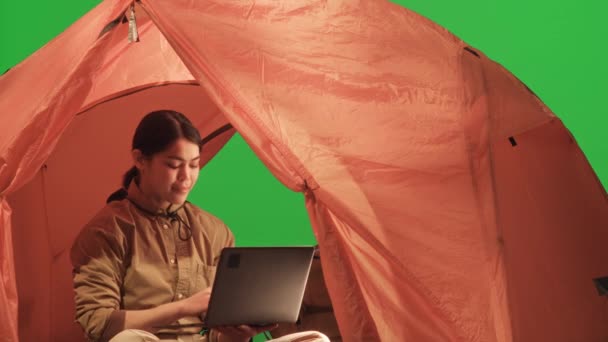 年轻的女游客坐在绿色色彩艳丽的帐篷里 喝着旅行杯子里的茶 在笔记本电脑上打字 — 图库视频影像