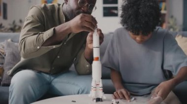 Afrikalı Amerikalı baba ve küçük oğlunun evde roket modelini çekerken.
