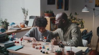 Neşeli Afrikalı Amerikalı adam, küçük oğluyla konuşuyor ve saçını dalgalandırıyor. Bu arada evde birlikte DIY güneş sistemi modeli yapıyorlar.