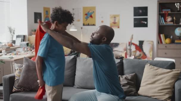 Afroamerykanin Ojciec Zakładając Czerwoną Pelerynę Małego Syna Podekscytowany Chłopiec Biegający — Wideo stockowe