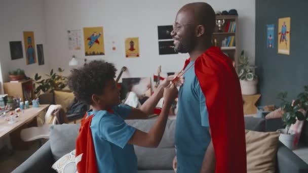 Mały Afroamerykanin Zakładając Pelerynę Superbohatera Tatę Następnie Biegając Nim Salonie — Wideo stockowe