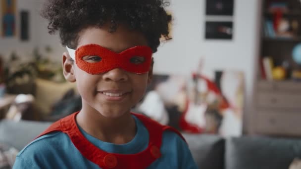 小さなアフリカ系アメリカ人の男の子の肖像画は 自宅で遊んでいる間 カメラを見て笑顔でスーパーヒーローの格好をした — ストック動画