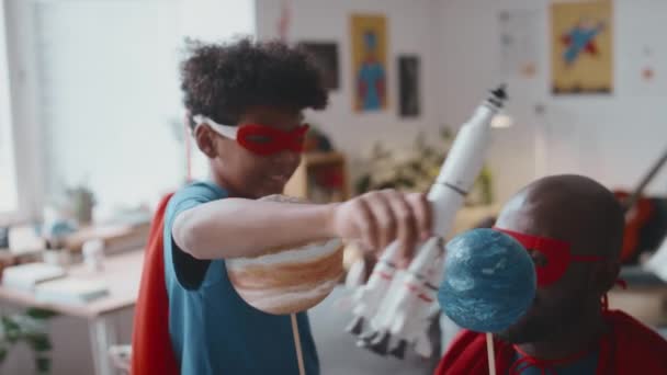 スーパーヒーローキャップとマスクで遊ぶジョイスアフリカ系アメリカ人の少年は 自宅で楽しんでいる間 父親が保有する惑星間の飛行を模倣するおもちゃロケットで遊びます — ストック動画